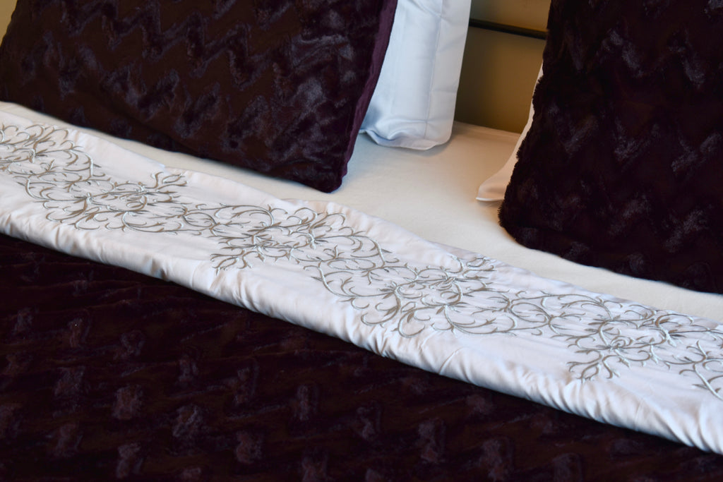 Close-up of a bed with floral-patterned white comforter and dark brown pillows.