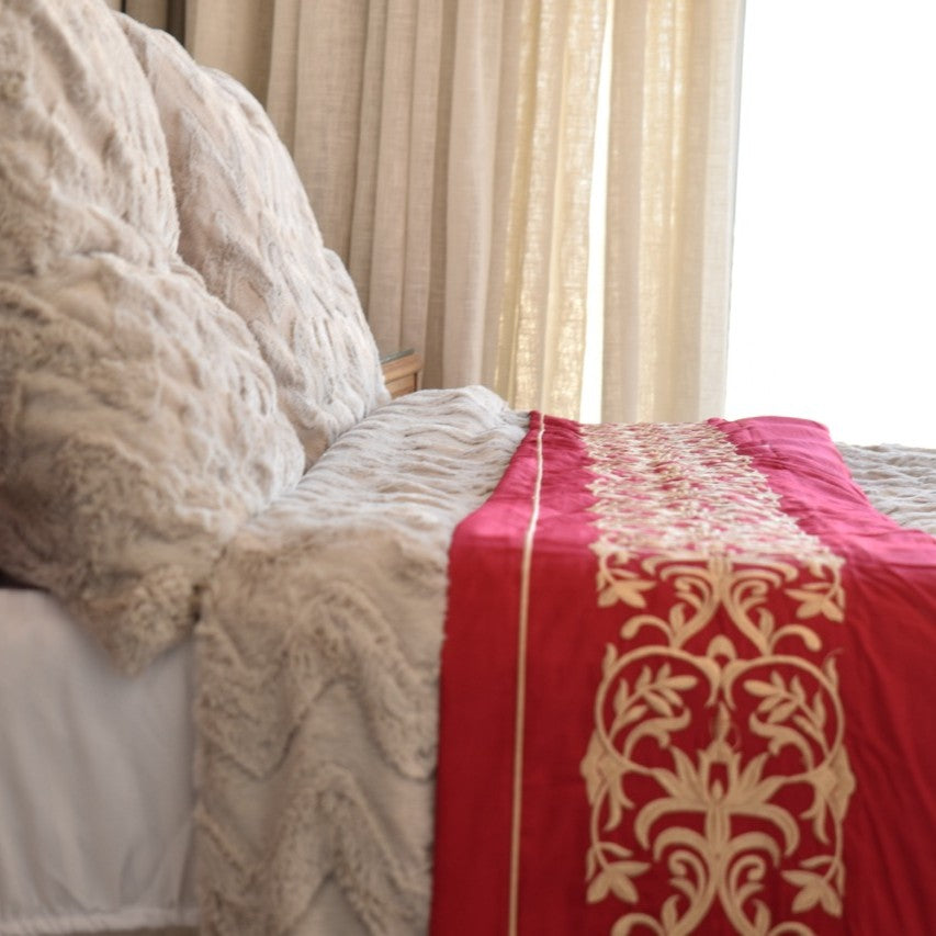 Close-up of a bed with lace bedding and a red decorative blanket.