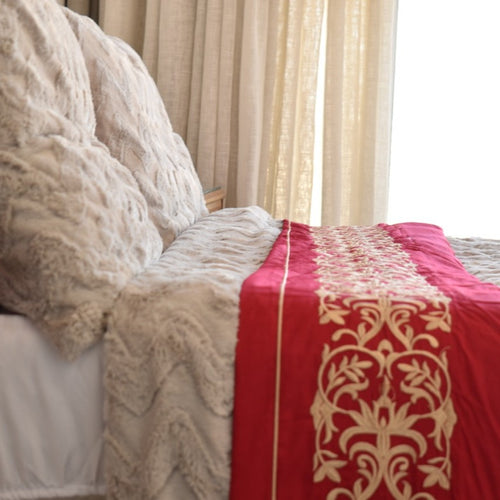 Close-up of a bed with lace bedding and a red decorative blanket.